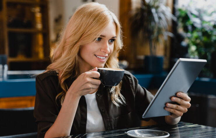 Young caucasian businesswoman using tablet for remote work, e-learning, e-commerce, e-banking, surfing social media online while drinking coffee in cafe restaurant
