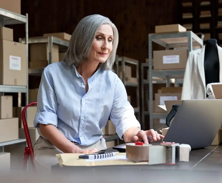 Mature female seller using computer checking ecommerce clothing orders. Global E-Commerce Solutions